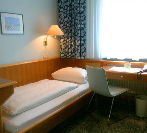 Ein einfaches Schlafzimmer mit einem Einzelbett, Schreibtisch und Fenster mit Vorhängen.