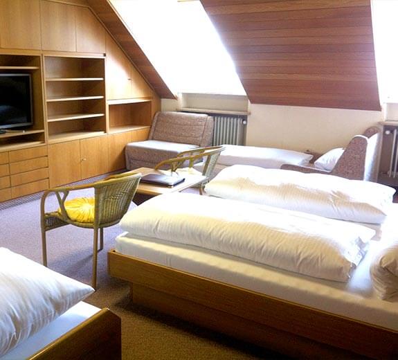 Ein gemütliches Zimmer mit zwei Betten, einem Sofa, einem Tisch und Regalen unter einer schrägen Decke.